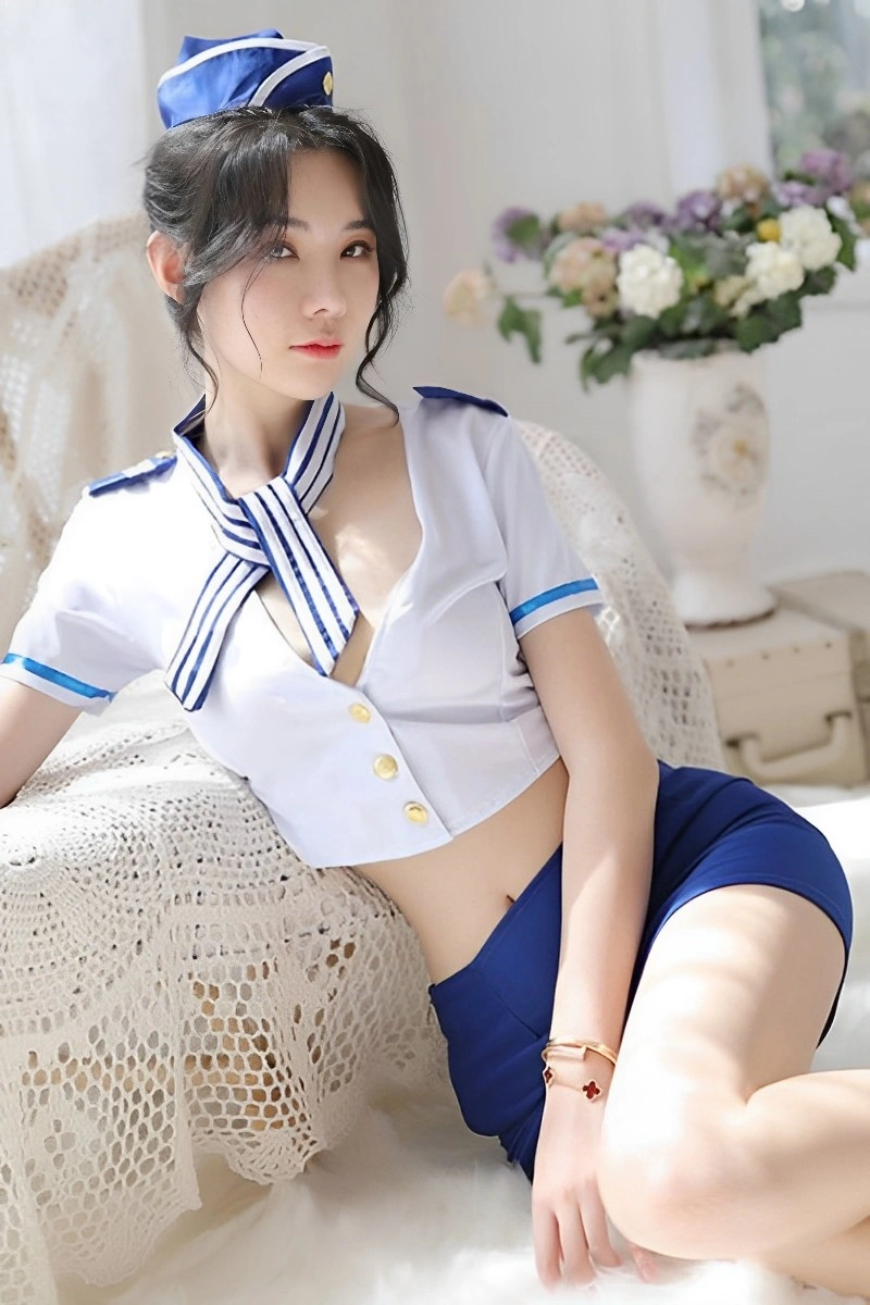 Model sitting in a Cabin Crew Cosplay Outfit featuring a plunging white top, blue skirt, and striped necktie.