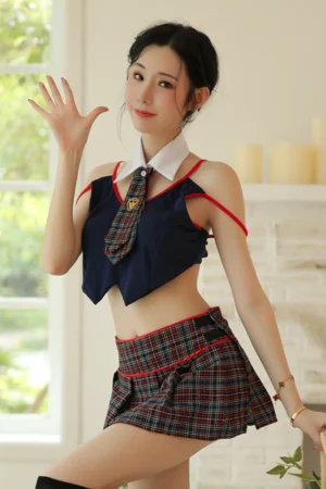 Model dressed in a b2b JK pleated skirt outfit featuring a plaid mini skirt, navy top with red trim, and school-style tie.