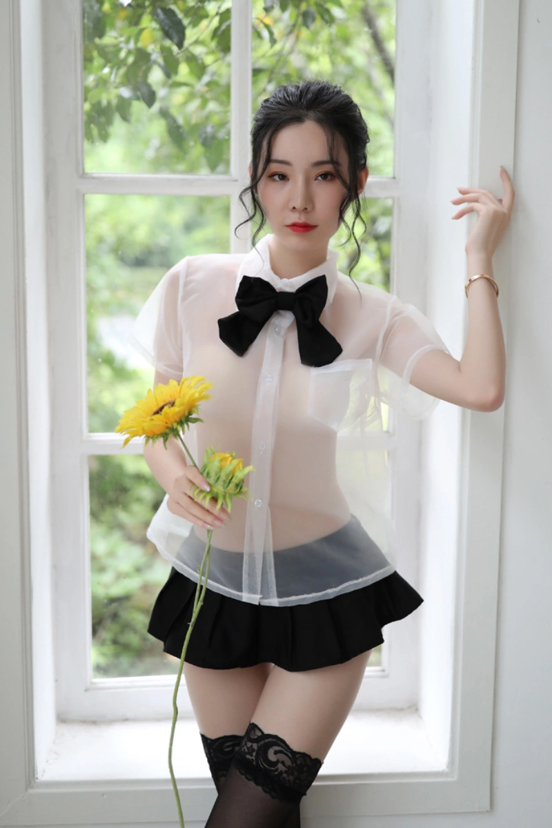 Model in b2b student fantasy lingerie wearing a sheer white blouse with black bow and pleated mini skirt