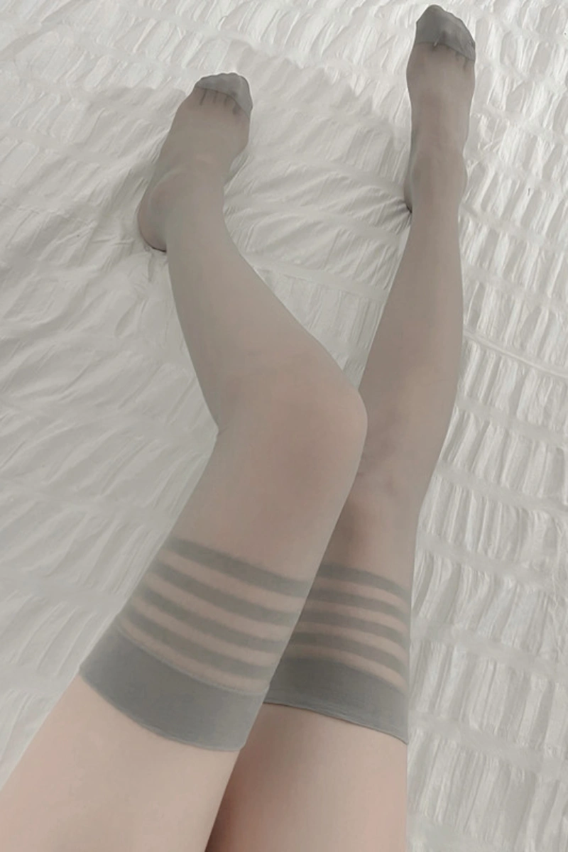 Model lying on bed wearing gray wholesale silk thigh high stockings with striped detail