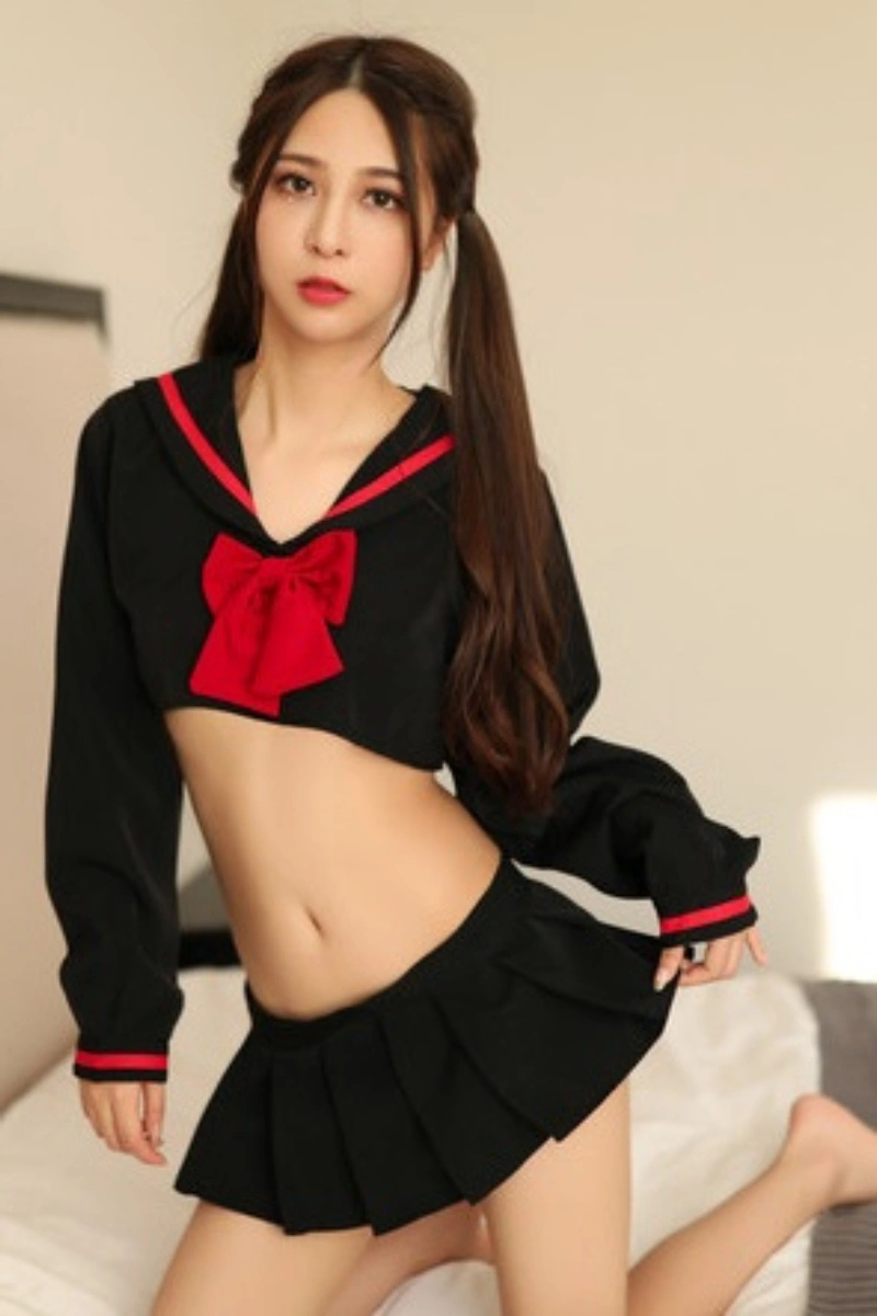Model in JK school uniform costume featuring a black cropped top with sailor collar and red bow, matched with a pleated black mini skirt.