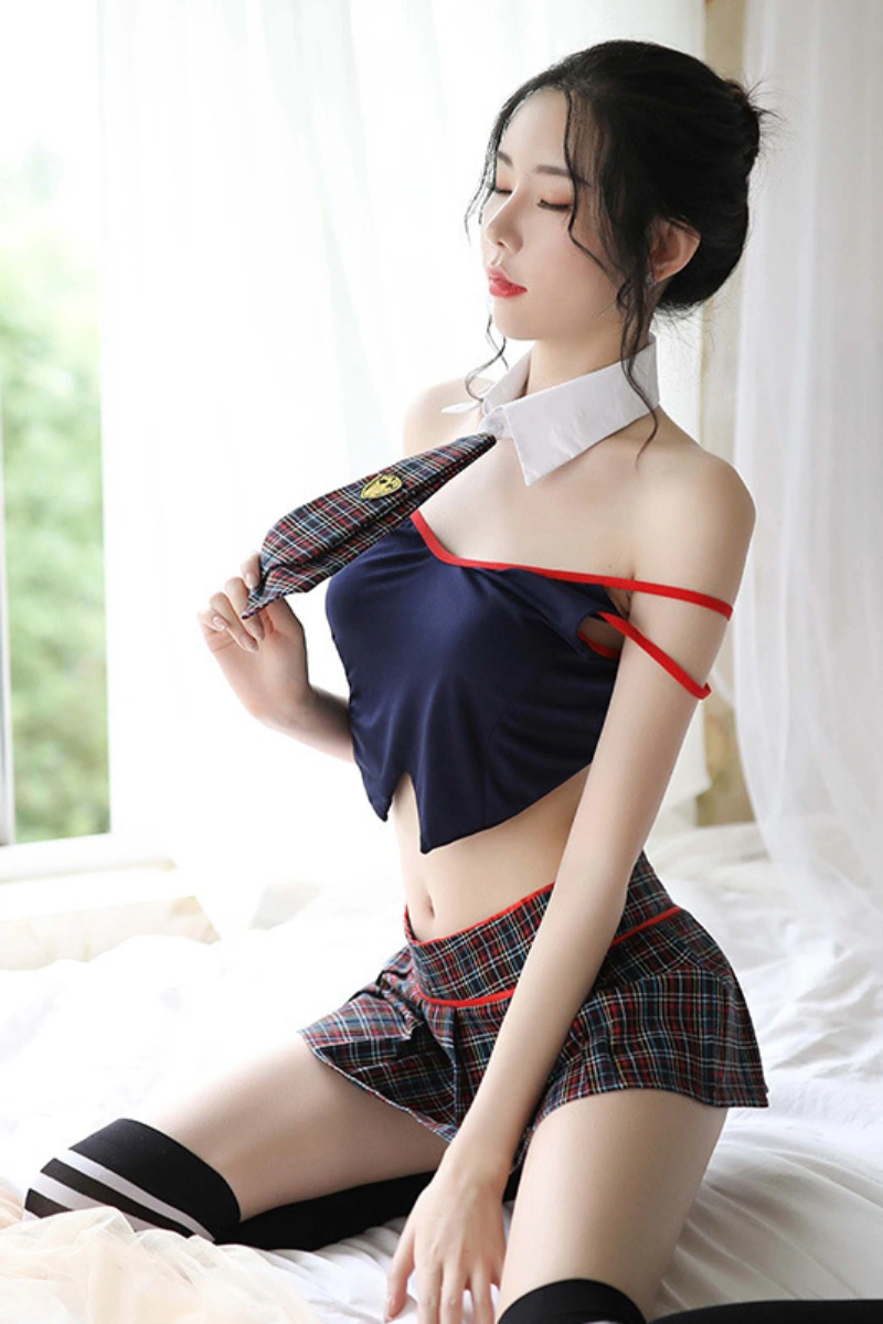 Model posing in a b2b JK pleated skirt outfit with a navy halter top, plaid mini skirt, and matching tie collar.