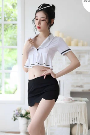 Model wearing Sexy Airline Girl Costume with short white crop top, scalloped black mini skirt, and matching hat.