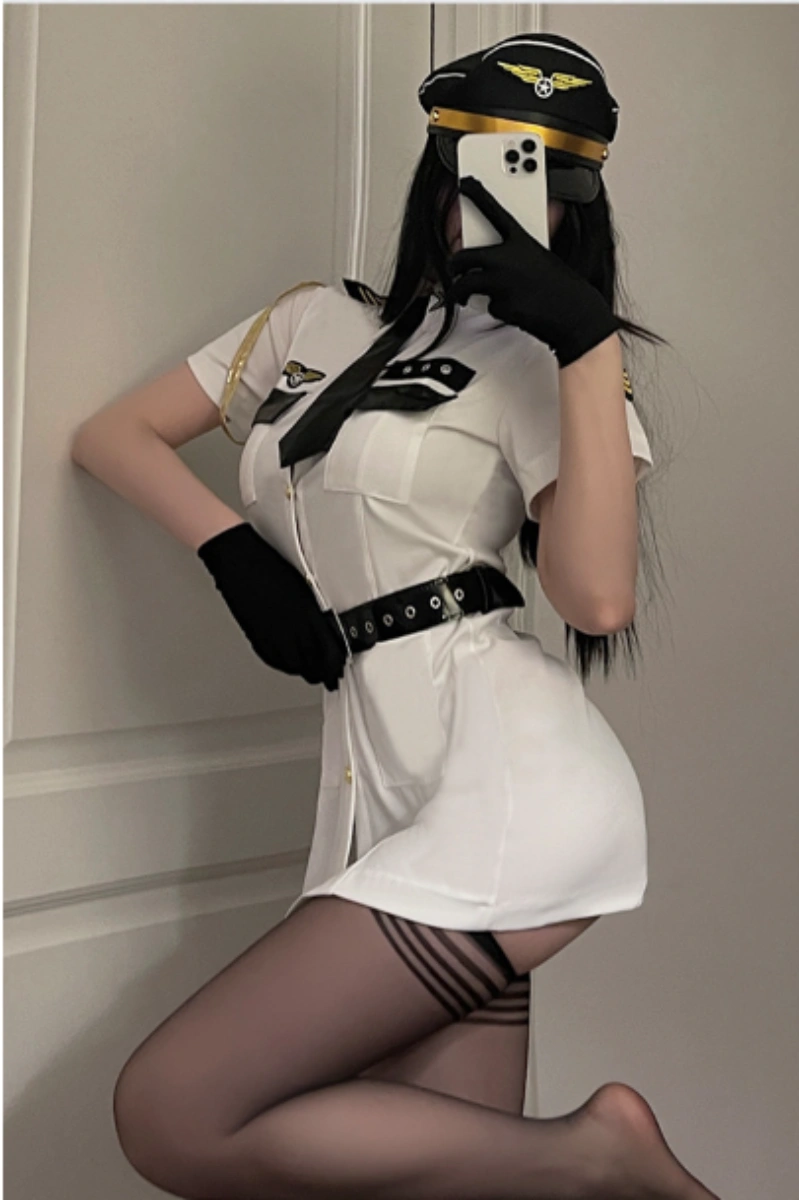 Model wearing Sexy Flight Uniform Dress in white with a belted waist, black gloves, and captain hat.