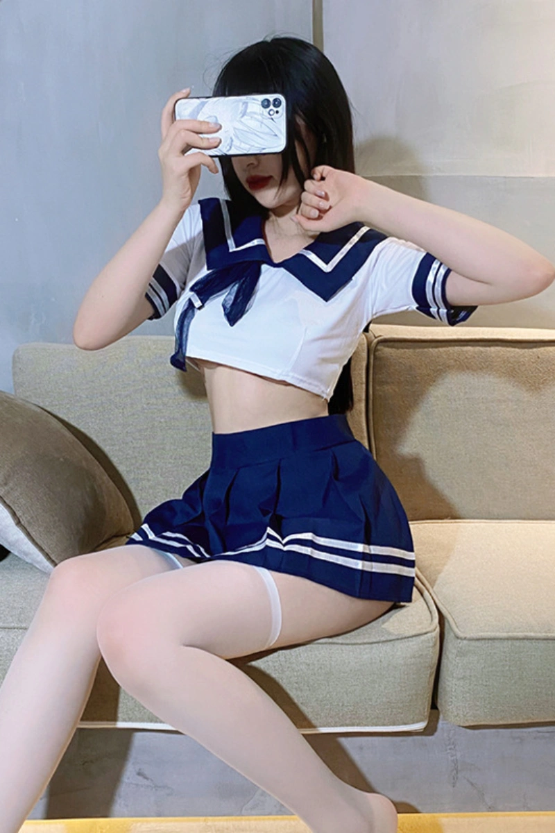 Model wearing sexy sailor schoolgirl outfit featuring short navy skirt, matching collar, and white crop top