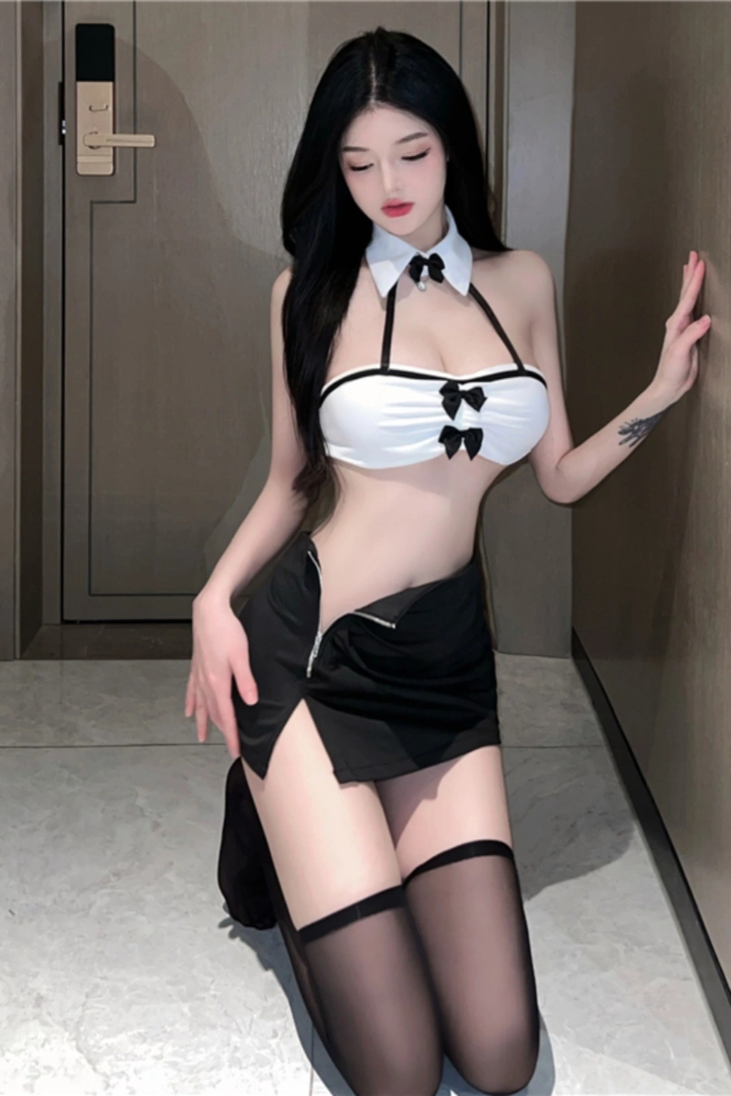 Model kneeling in a wholesale sexy secretary uniform featuring a white crop top with black bow accents and a black mini skirt.