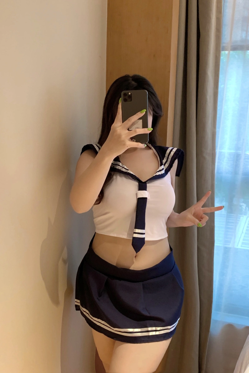 Sexy student costume with white sleeveless sailor top, tie, and navy pleated skirt.