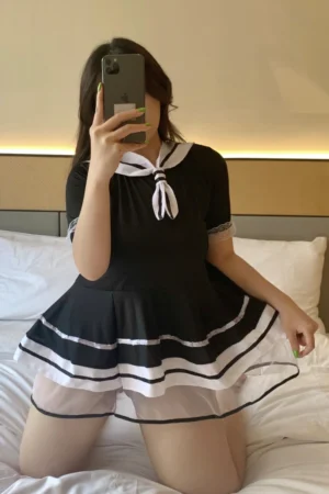 A student costume with black mini dress, white sailor collar, and sheer layered hem, shown seated.