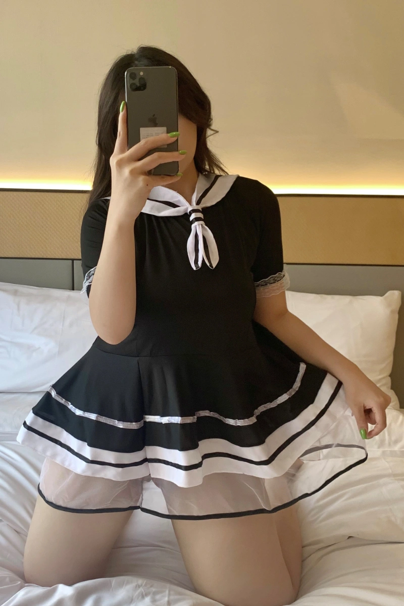 A student costume with black mini dress, white sailor collar, and sheer layered hem, shown seated.