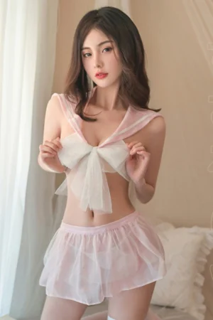 Model in pink wholesale student costume featuring a sheer sailor collar top with oversized bow and pleated mini skirt.
