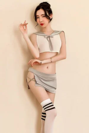 Model posing in wholesale schoolgirl uniform outfit with silver mini skirt, strappy sides, and a white cropped sailor top with silver bow