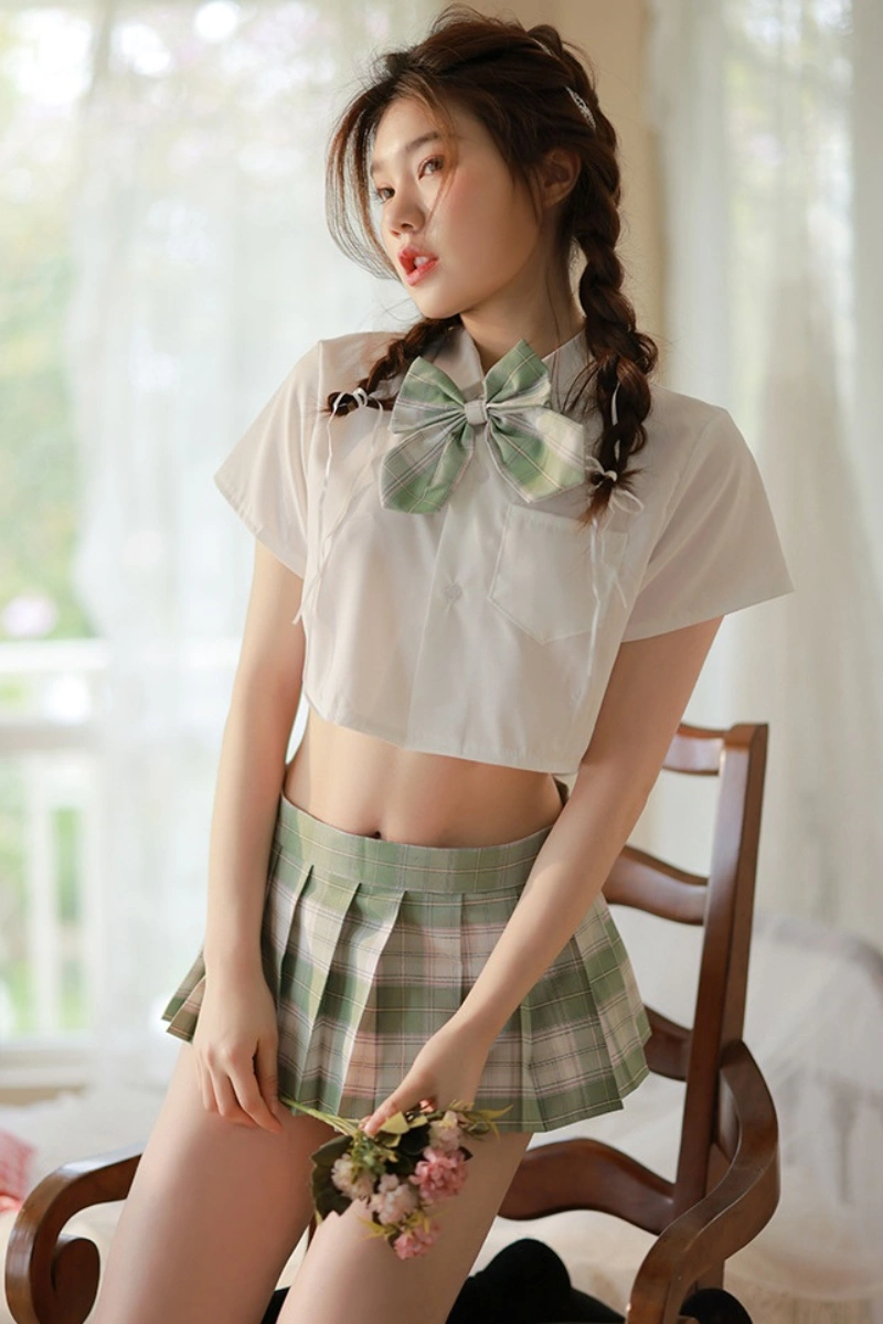 Female model in a b2b JK mini skirt costume featuring a green plaid pleated skirt, green bow, and cropped white shirt.