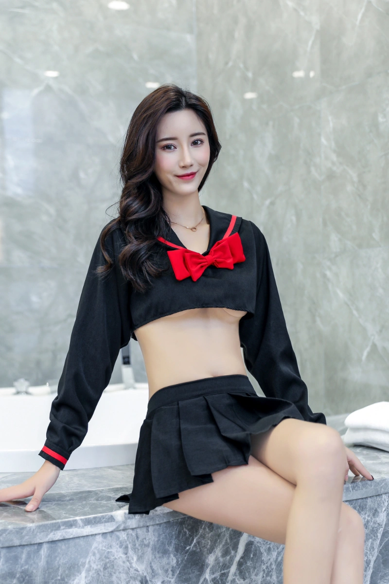 Model wearing b2b sexy classroom girl costume featuring a cropped black sailor-style top with a bold red bow and pleated mini skirt.