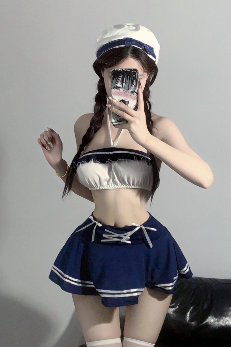 Model wearing b2b student lingerie featuring a navy pleated mini skirt and white halter crop top with matching hat