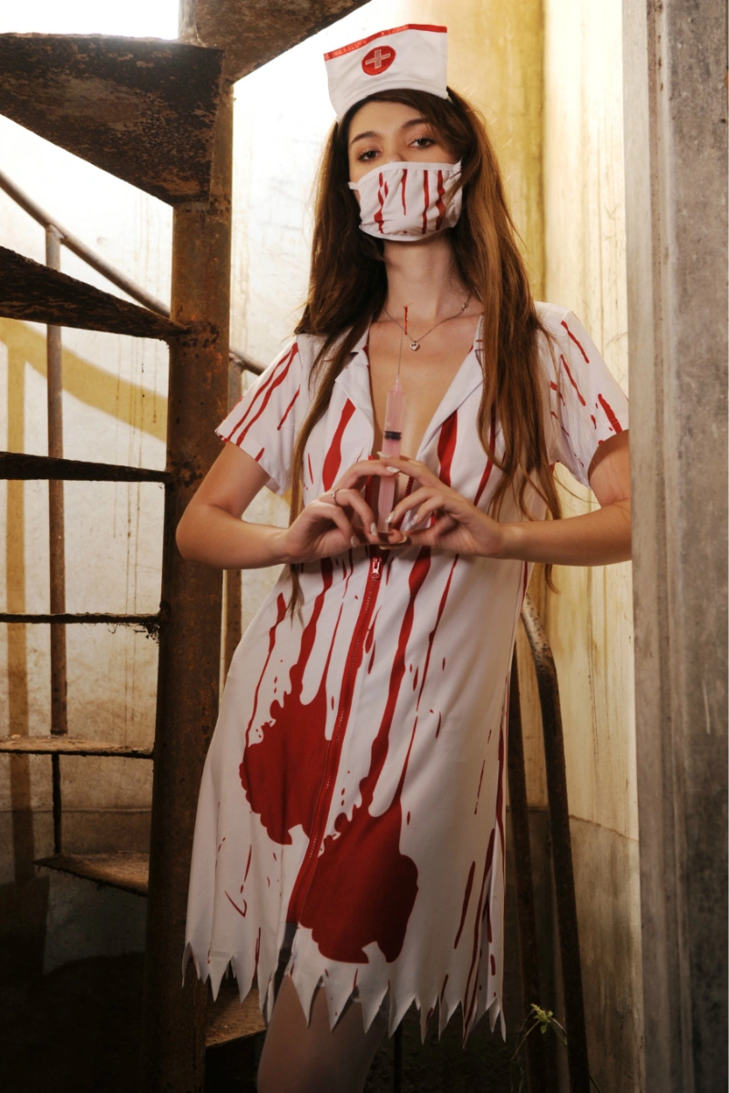 Model wearing a Bloody Nurse Costume with blood print dress, nurse hat, and mask, holding syringe.