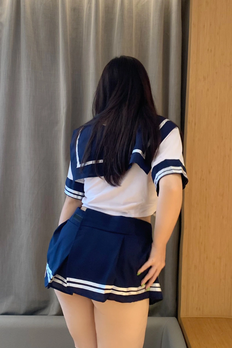 Back view of sexy schoolgirl lingerie showing pleated navy skirt and cropped sailor blouse.