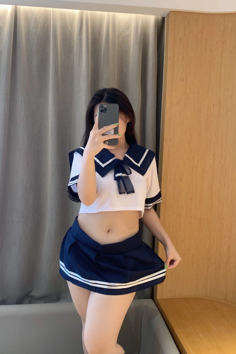 Model posing in sexy schoolgirl lingerie set with cropped sailor top and pleated skirt.