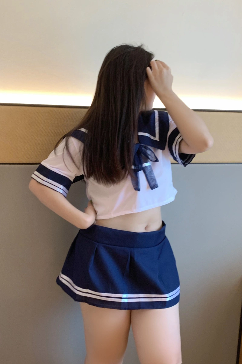 Model wearing sexy schoolgirl lingerie featuring a navy pleated skirt and cropped sailor top.