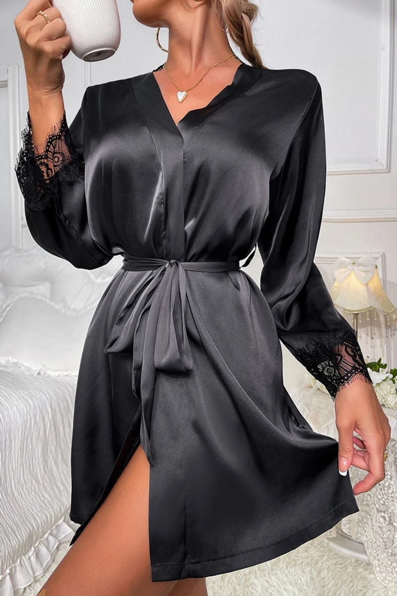 Model wearing a b2b sexy black nightgown made of smooth satin fabric with lace-trimmed cuffs, V-neck design, and adjustable waist tie in an elegant bedroom setting.