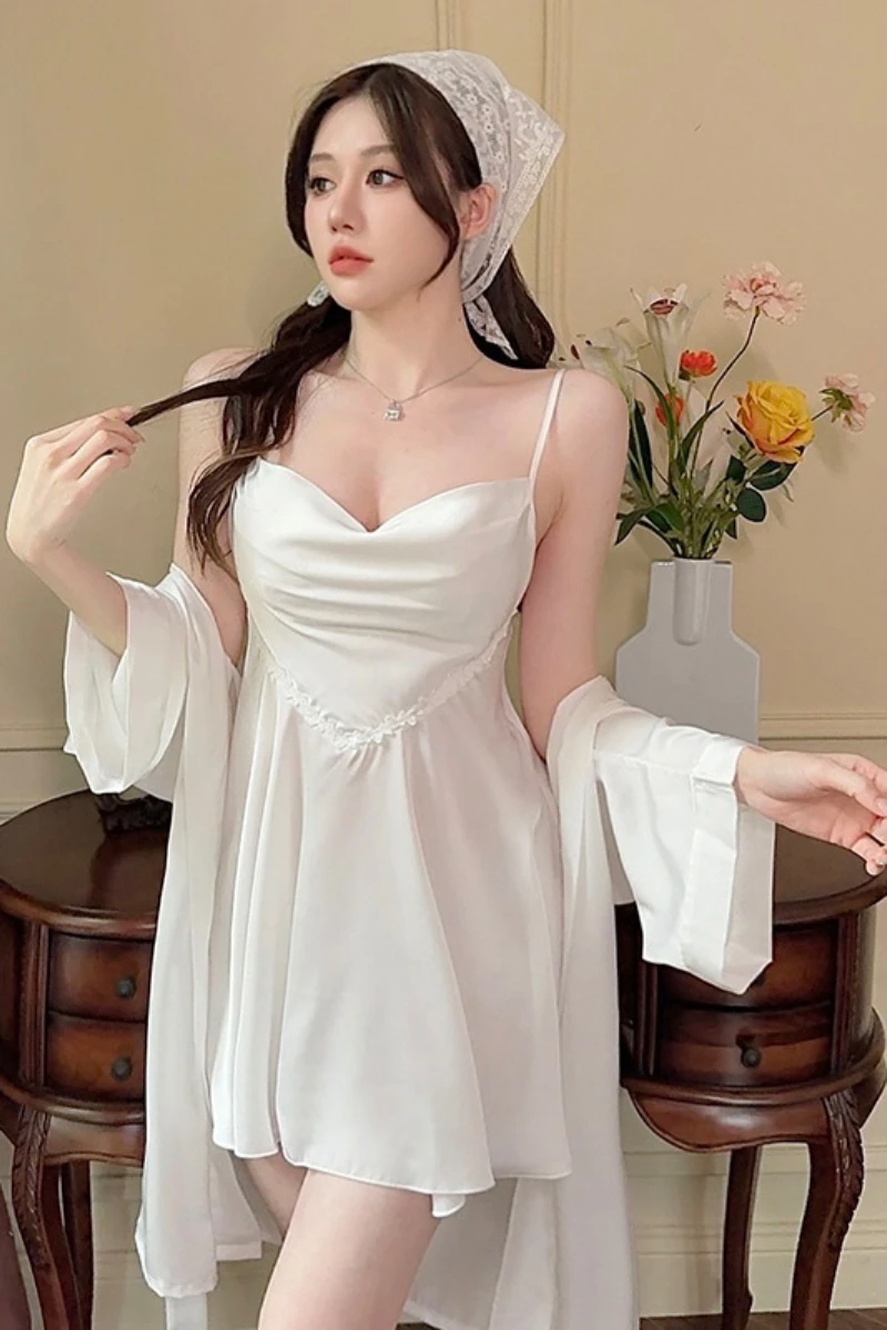 Model wearing a white custom womens sexy nightgown featuring a draped satin bust, adjustable straps, and matching sheer robe in a bedroom setting