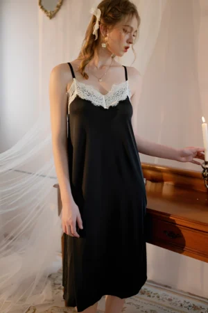 Model wearing a black lace trim satin pajama set featuring a smooth satin body and delicate lace neckline in a bedroom setting